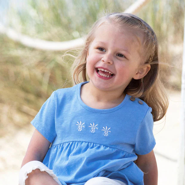 Young girl in a blue dress sitting on sand with a blurred natural background