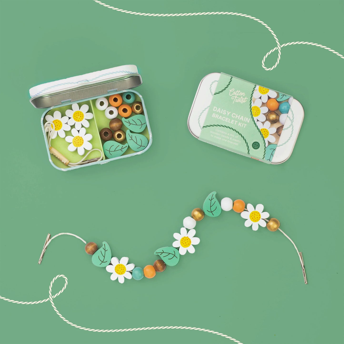 Two small metal tins of bead串 on a mint green background, with a decorative bead strand laid out in front. The beads include white daisy flowers with yellow centers, mint green leaves, white and orange round beads, and some larger brown beads.