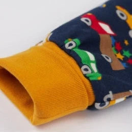 Close-up of a children's long-sleeve top or sweatshirt cuff, showing a navy blue fabric printed with colorful cartoon vehicles and a wide ribbed mustard yellow cuff.