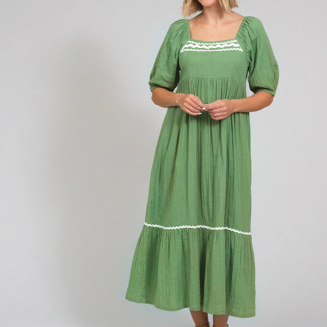 Woman wearing a green dress with white trim on a plain background