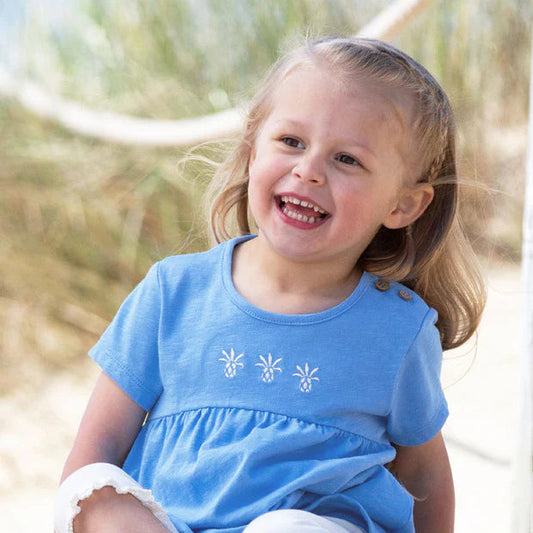 Young girl in a blue dress sitting on sand with a blurred natural background