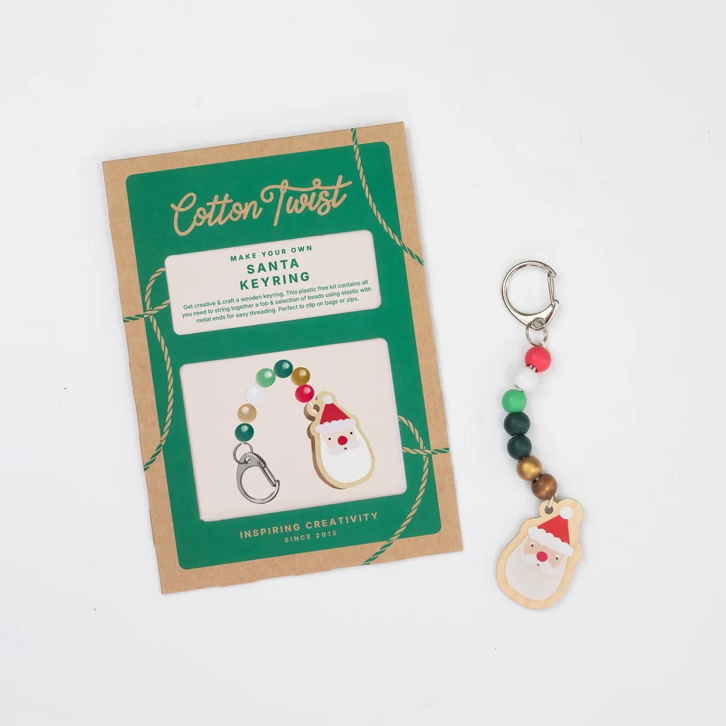 A handmade Santa keyring charm with colorful beads and a wooden Santa face charm, displayed next to its green and kraft paper packaging card on a white background.