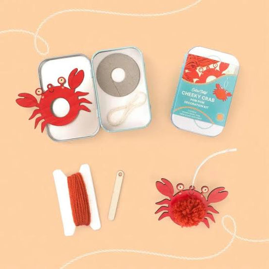 Cheeky Crab pom pom decoration kit with crab-shaped item, yarn, and packaging on a beige background