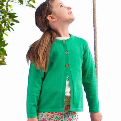 Child in a green jacket and floral pants standing on a swing in a natural setting