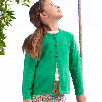 Child in a green jacket and floral pants standing on a swing in a natural setting