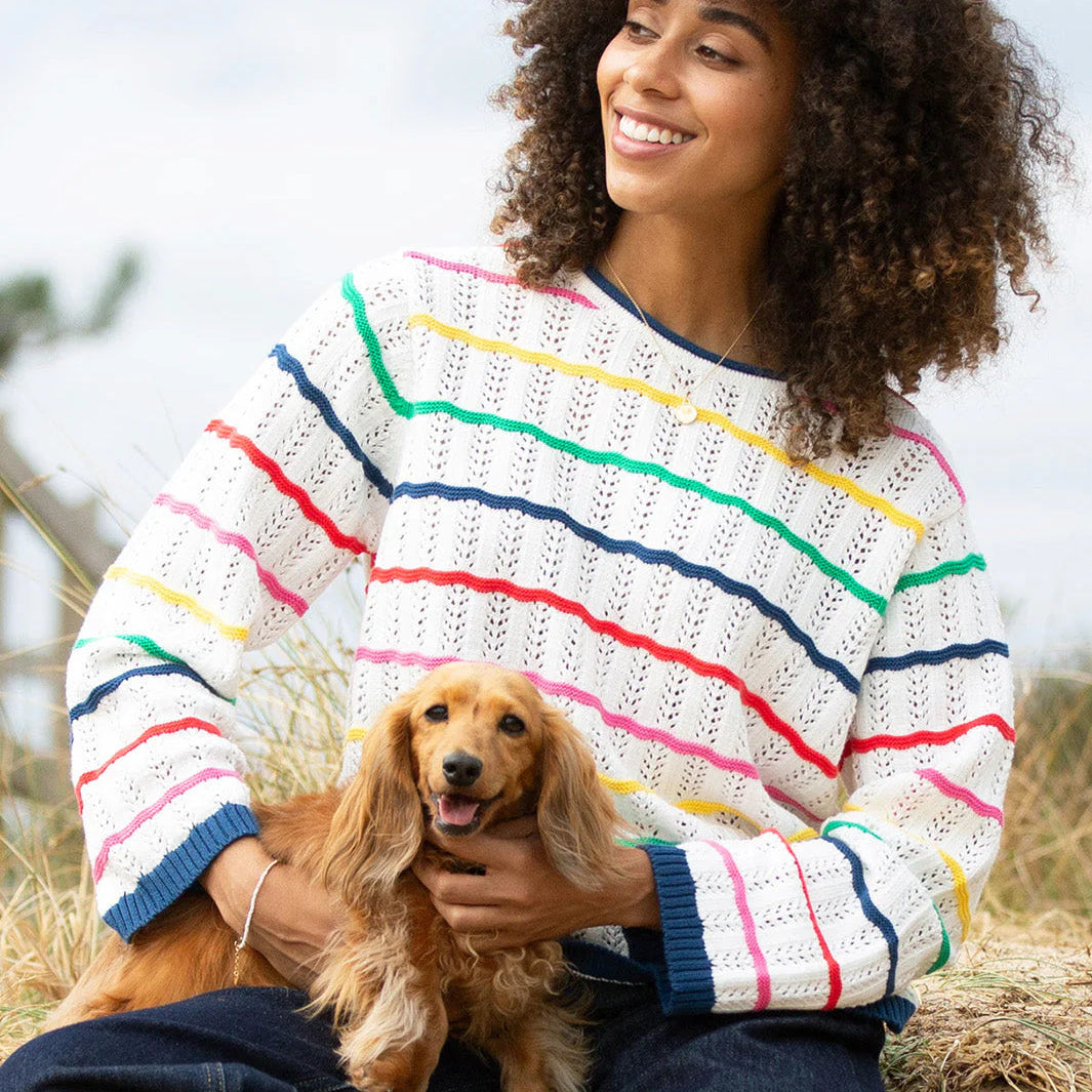 Woman wearing a colorful striped sweater holding a small dog outdoors.