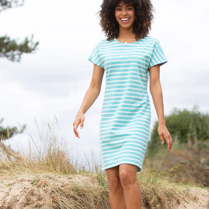 A woman wearing a short-sleeve, knee-length striped dress in mint green and white stands on a sandy dune outdoors under an overcast sky.