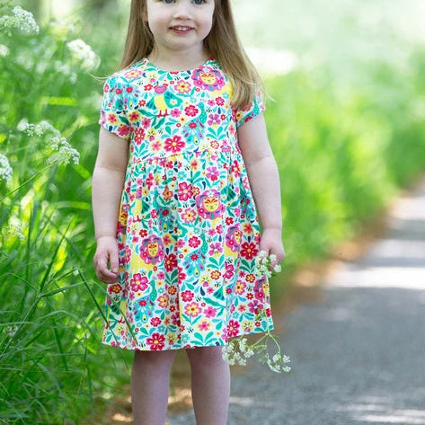 Young girl in a colorful floral dress standing on a path surrounded by greenery.
