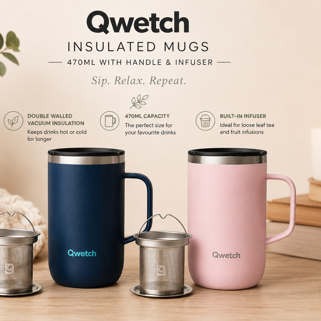 Two Qwetch insulated mugs, one navy blue and one light pink, displayed on a wooden surface with a small metal infuser basket in front of each. The background is a warm beige with decorative props including a potted plant, a textured throw blanket, and a candle.