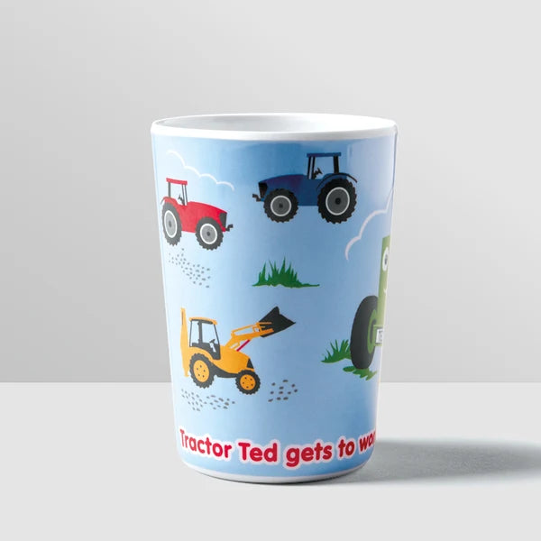 A tall white ceramic mug with a light blue printed design featuring cartoon tractors and construction vehicles on a grassy field, with red text at the bottom.